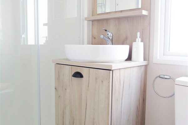 Small modern bathroom with a light wood vanity, white vessel sink, chrome faucet, wall mirror, and glass shower enclosure. More: toilet visible on the right.