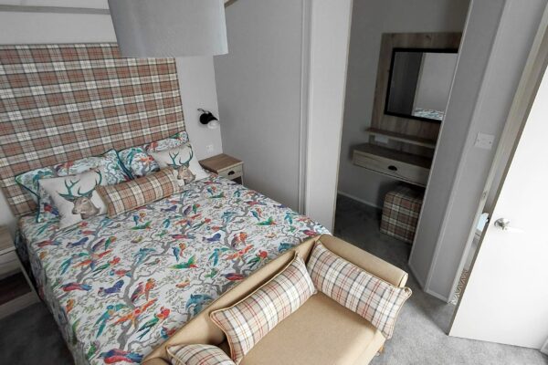Cozy bedroom with a double bed, plaid headboard, and colorful bird-pattern bedding with matching pillows.