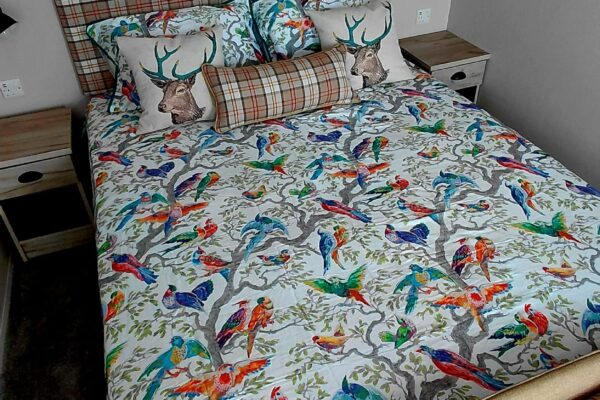 Bed with a colorful bird-pattern duvet, plaid headboard, and decorative deer-themed pillows in a gray bedroom.
