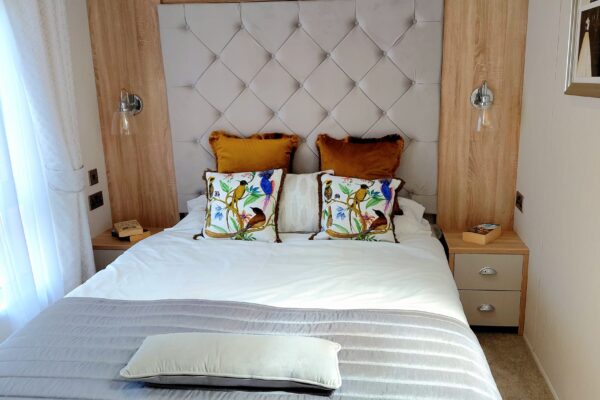 Queen bed with a gray tufted headboard, brown and bird-patterned cushions, and white bedding in a wood-panelled bedroom.